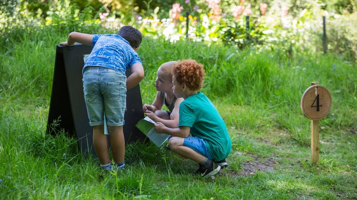 Three children reading a sign while doing an Easter activity trail in the grounds of Rufford Old Hall, Lancashire
